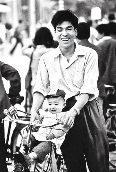 图为上世纪80年代骑着自行车带着孩子的爸爸露出幸福的笑容.
